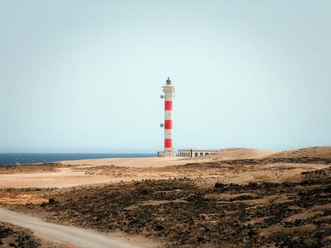 A solitary lighthouse with red stripes standing on a remote coastal landscape.