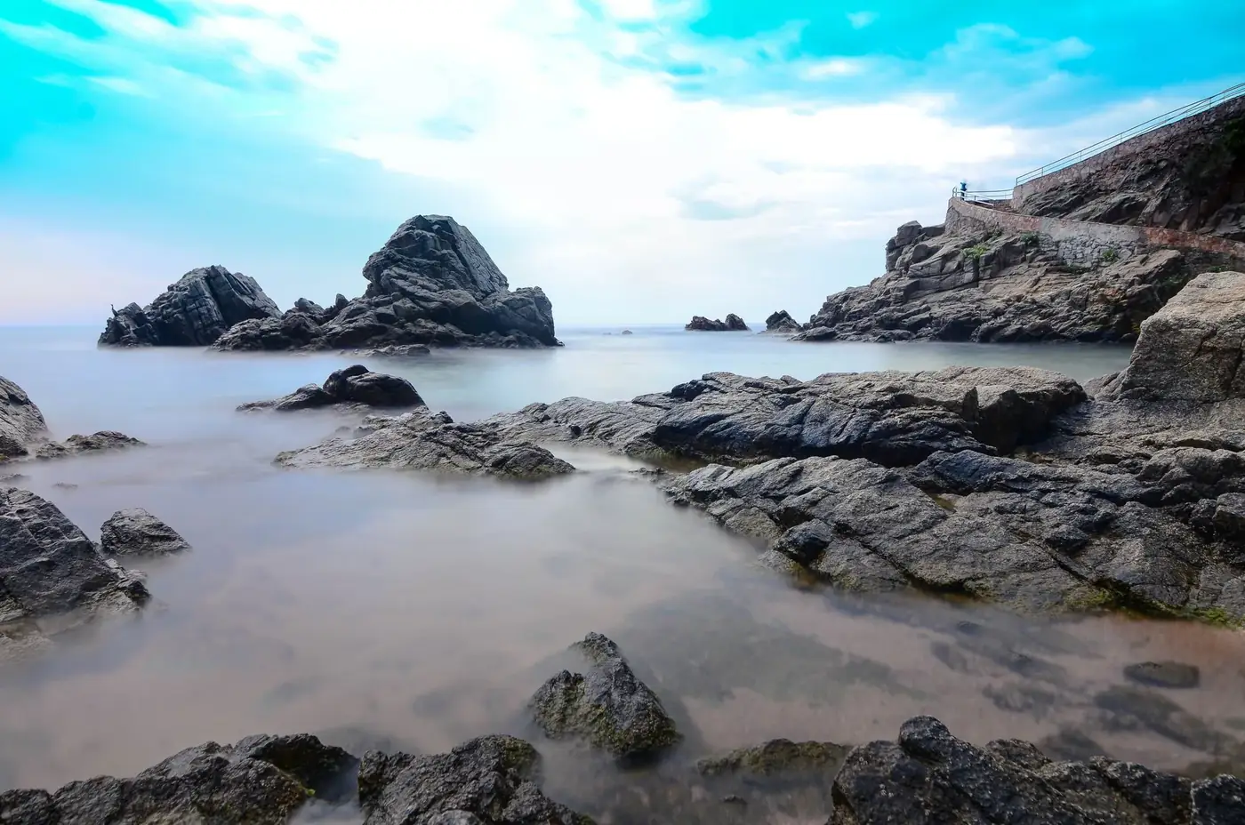 Long exposure shot of rocky coastline in Catalonia, Spain, with serene sea and blue sky.