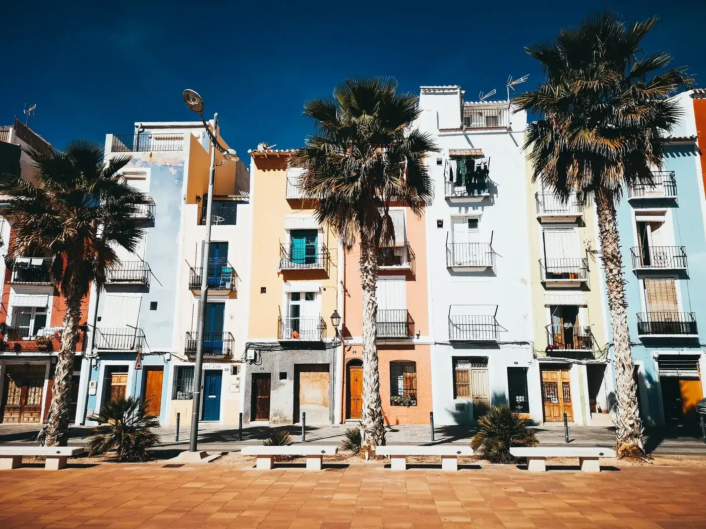 Vibrant pastel townhouses and palm trees line a sunny promenade in Villajoyosa, Spain.