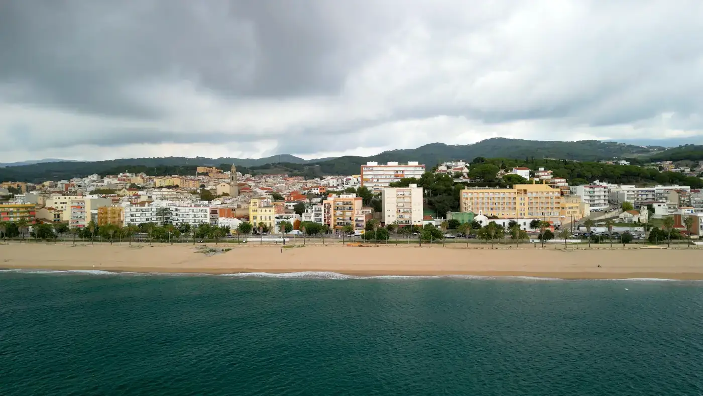 Aerial view of Canet de Mar beach with overcast sky and cityscape in the background.