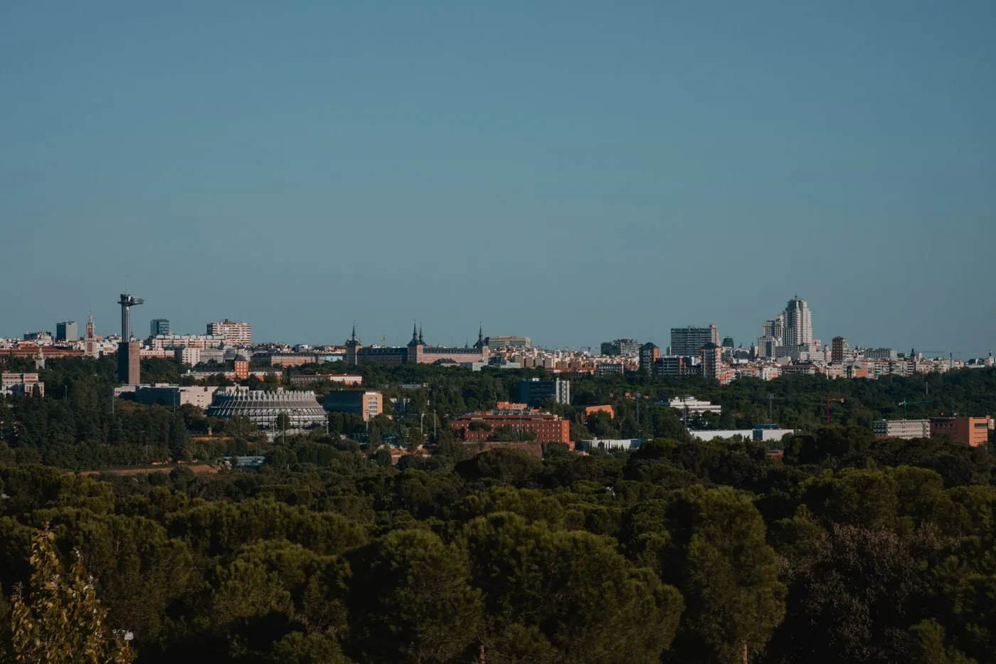 A scenic view of Madrid's cityscape with a forested foreground under a clear sky.