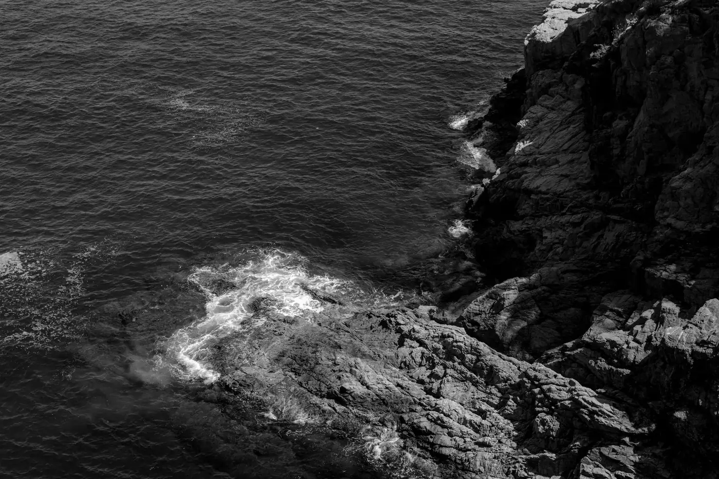 Dramatic black and white coastal cliff with ocean waves in Tossa de Mar, Spain.