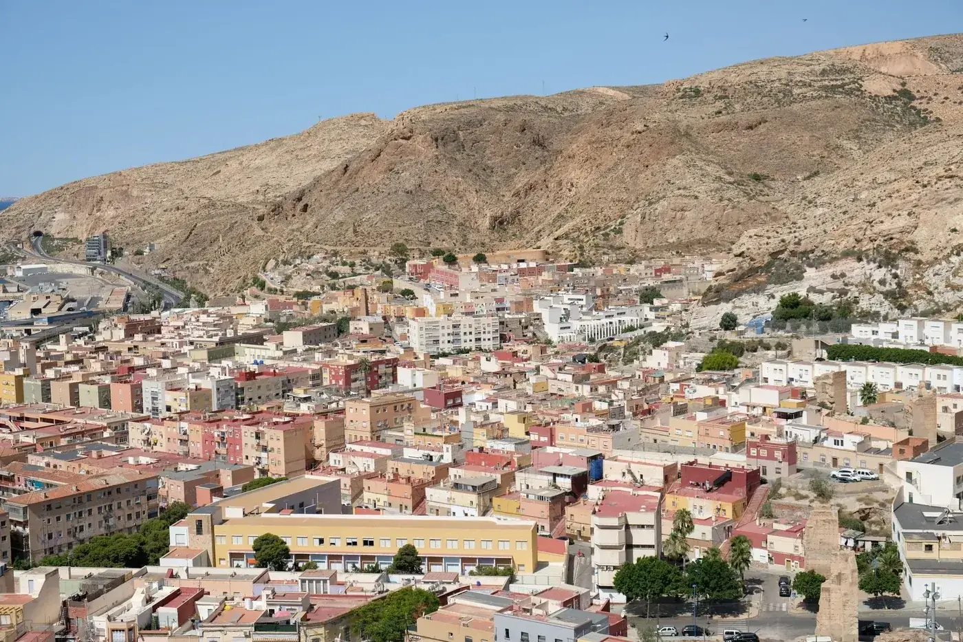 A breathtaking aerial view of a Spanish cityscape with hills and vibrant buildings under a clear blue sky.