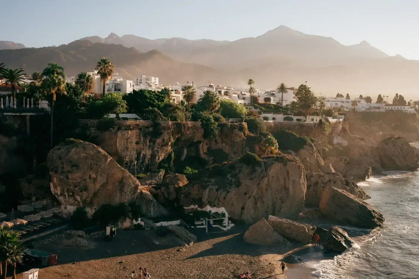 Stunning sunrise view of Nerja's rocky coastline and white buildings with mountains in the background.
