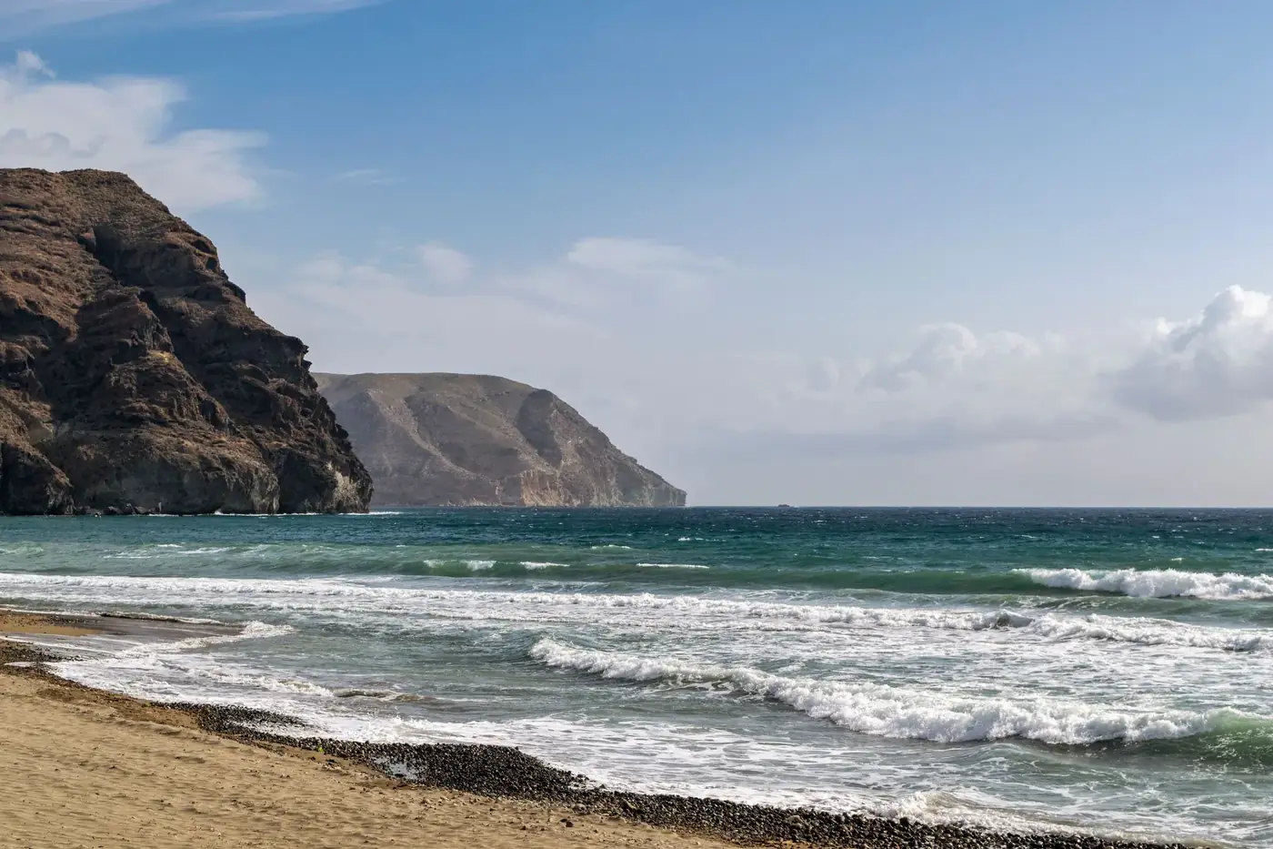 Beautiful coastal landscape of Las Negras beach with waves and rocky hills under a clear summer sky.