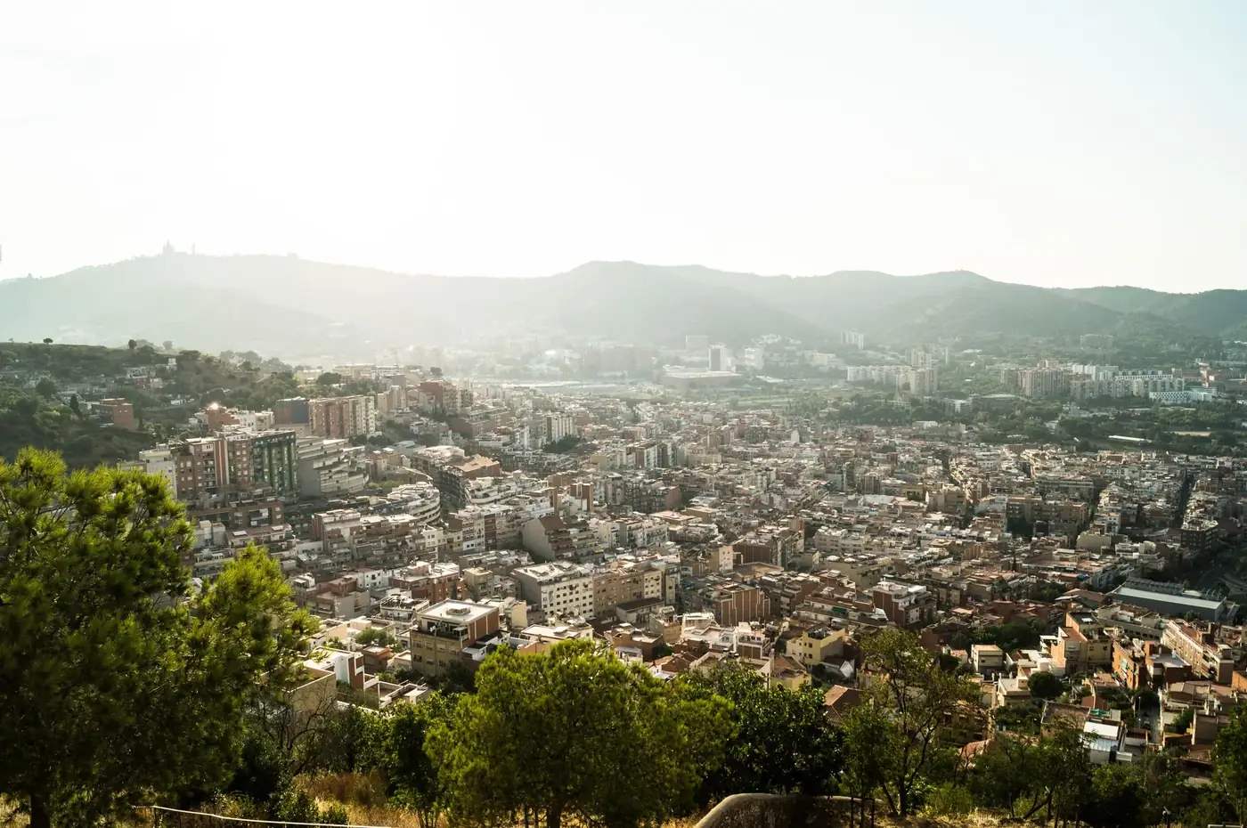 Aerial view capturing Barcelona's urban landscape surrounded by mountains and hills during daylight.