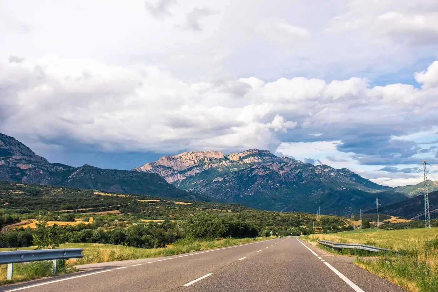 A scenic highway stretches across the vibrant Spanish countryside with mountains in the backdrop.
