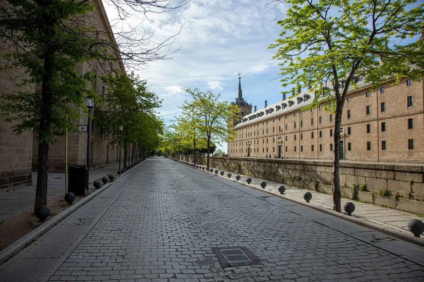 Empty street lined with trees and historic buildings at the Royal Site of San Lorenzo de El Escorial, Spain.