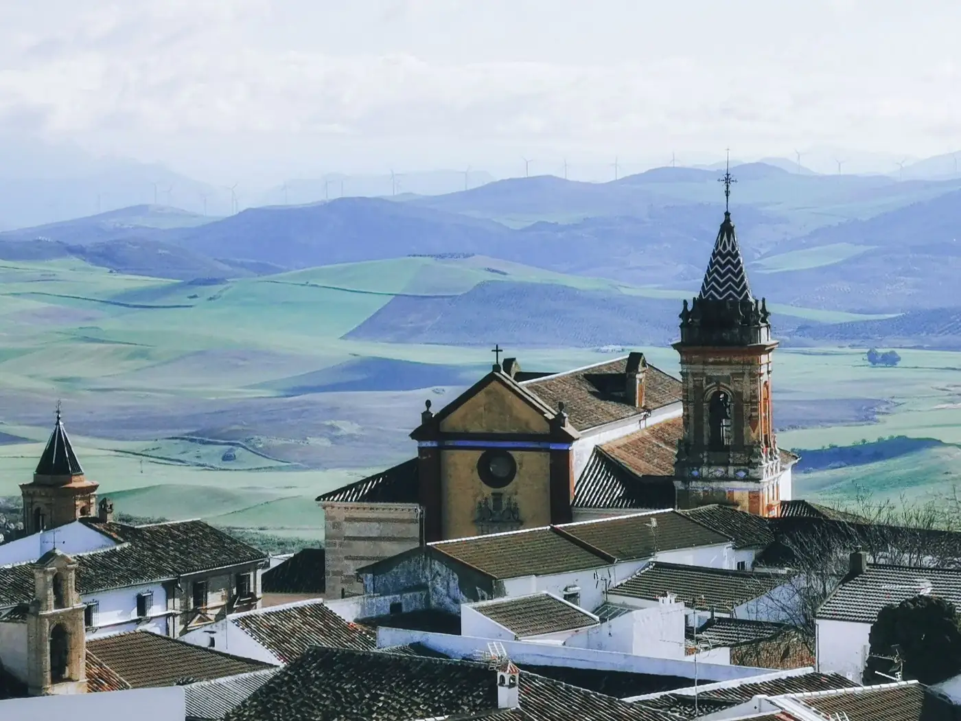 A scenic birds-eye view of a church with rolling hills and wind turbines in a tranquil summer landscape.