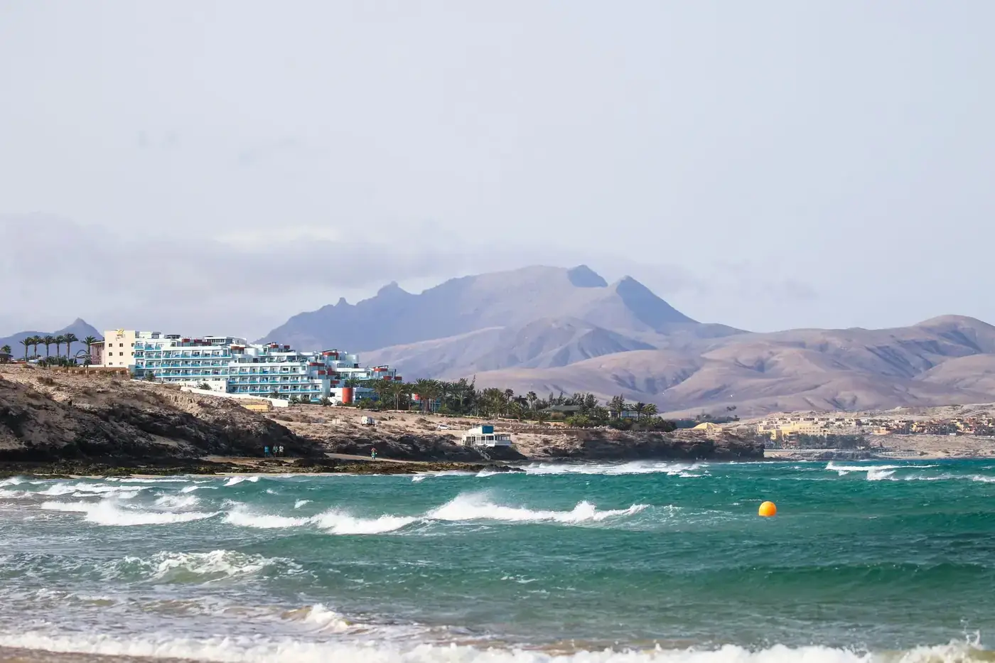 Scenic view of Fuerteventura coastline with waves and mountains in the background.