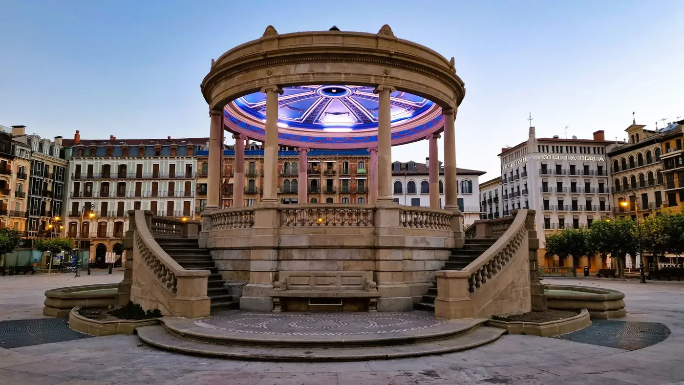 Elegant stone gazebo with illuminated ceiling in Pamplona's scenic plaza at twilight.