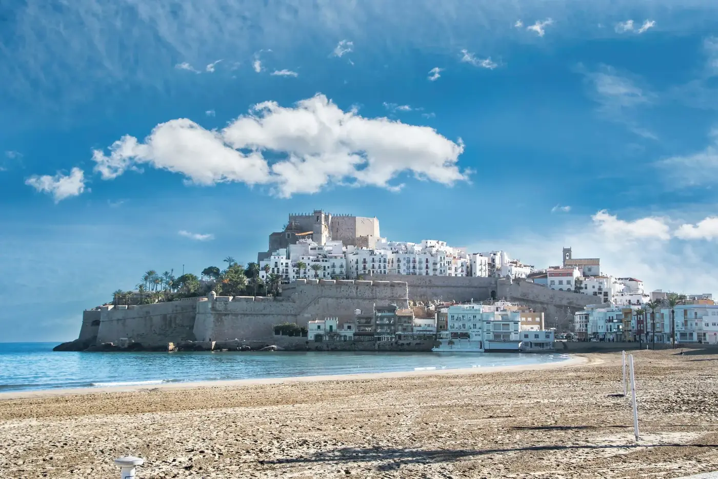 Picturesque coastal town with historic castle and sandy beach under blue skies.
