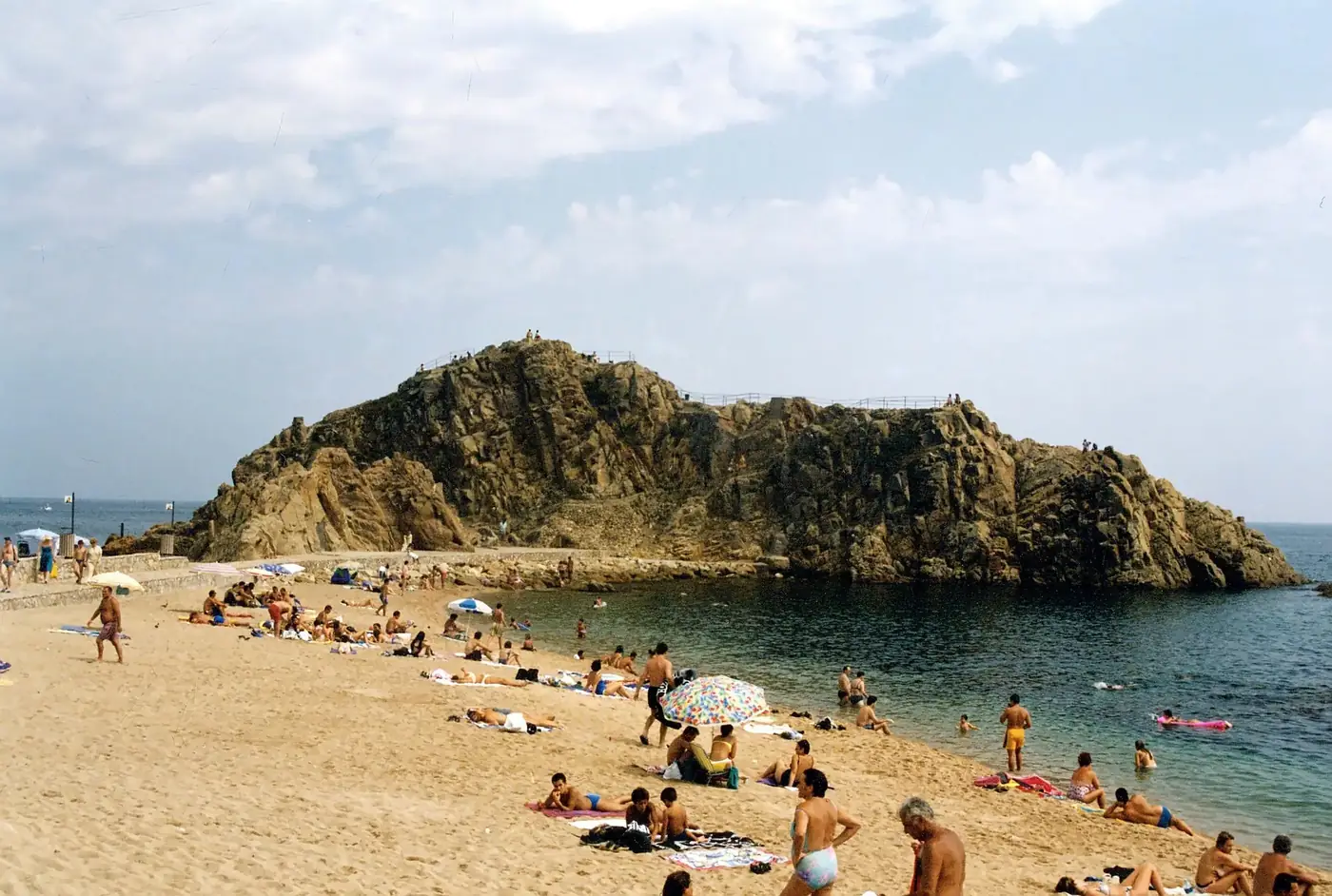 Crowded beach scene at Sa Palomera in Blanes, Spain on a sunny day.
