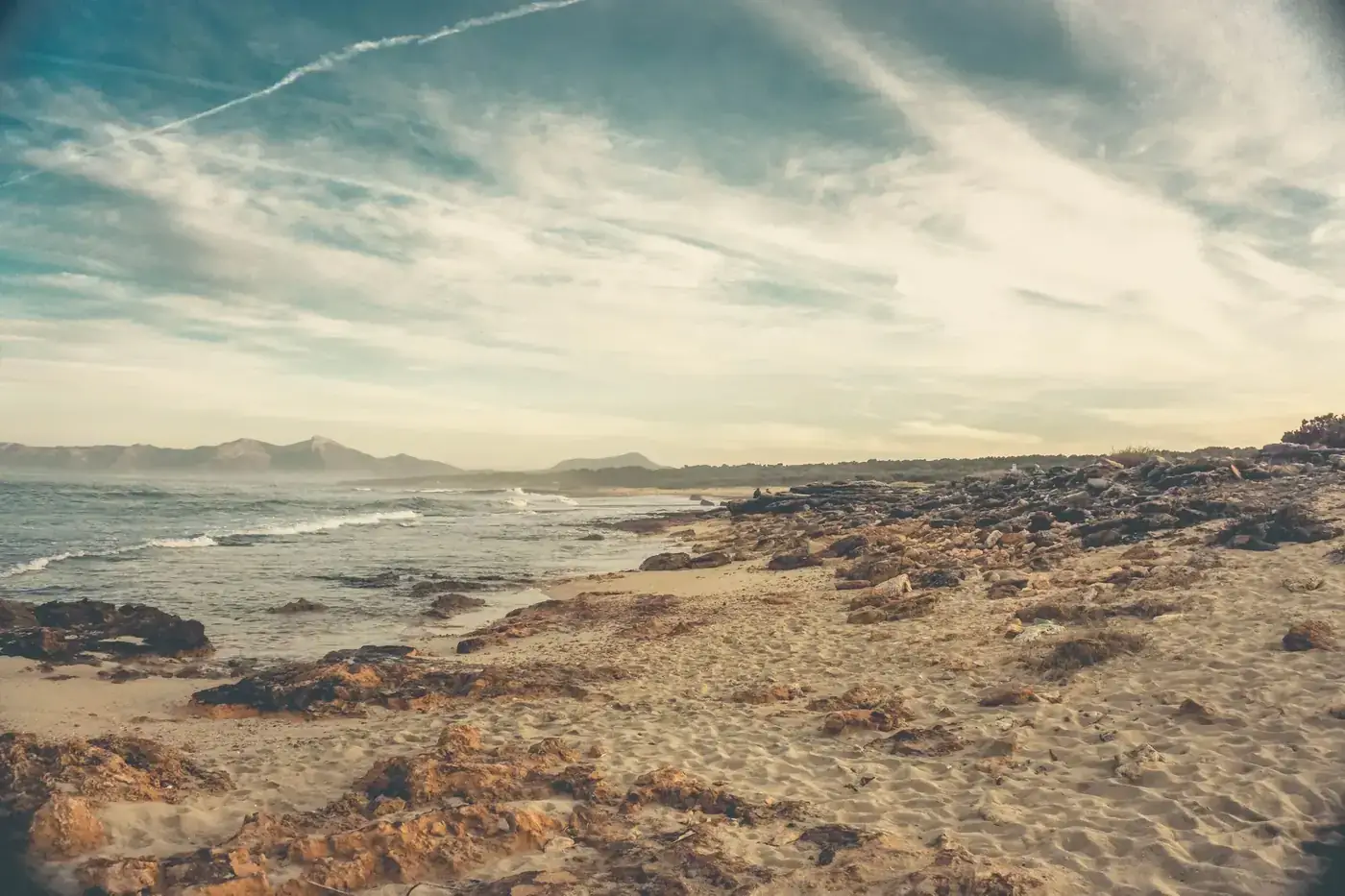 Scenic view of Santa Margarita beach in Spain, featuring serene waves and rocky shorelines at sunset.