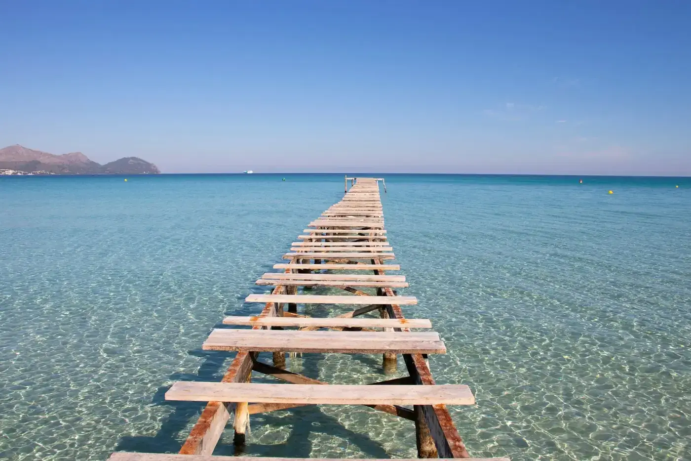 Serene wooden pier stretching into clear turquoise waters in Mallorca, Spain, under a bright blue sky.