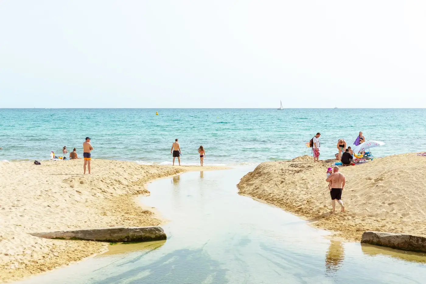 Tourists enjoying a sunny day on a sandy beach in IB, Spain, with clear blue waters.