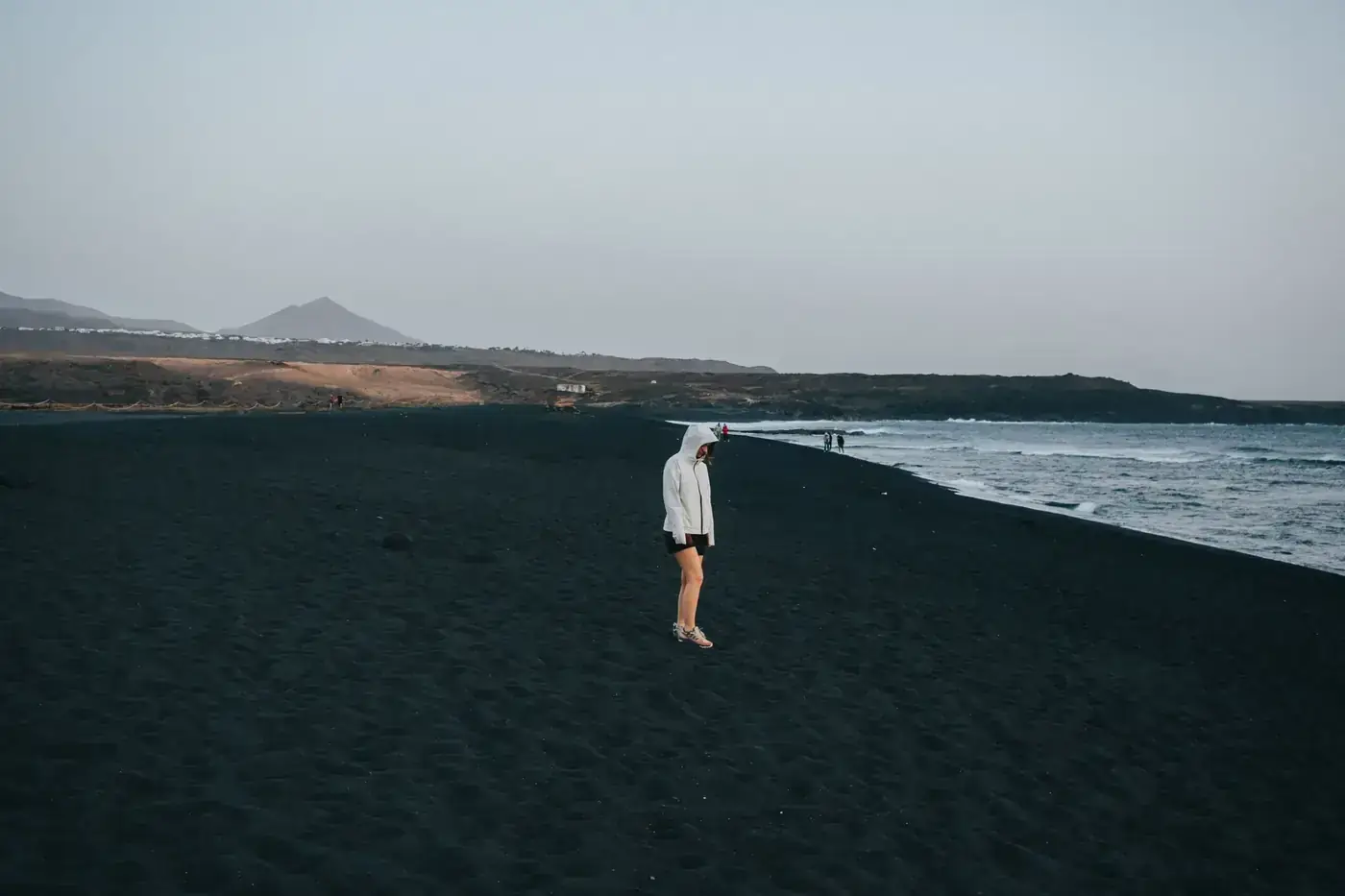 A person stands on the black sand beach of Lanzarote at dusk, highlighting serene coastal solitude.