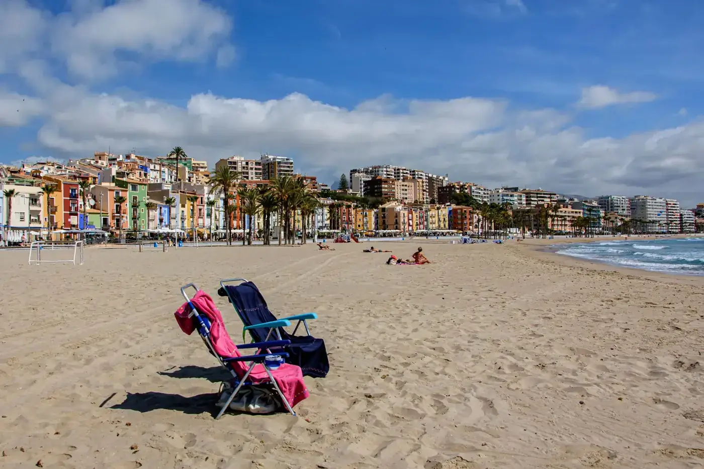 Sunny day on the sandy beach of Villajoyosa, Spain with vibrant buildings and chairs.