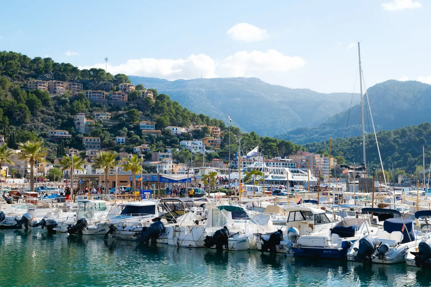 Vibrant marina at Port de Sóller with boats and hillside houses under a sunny sky.