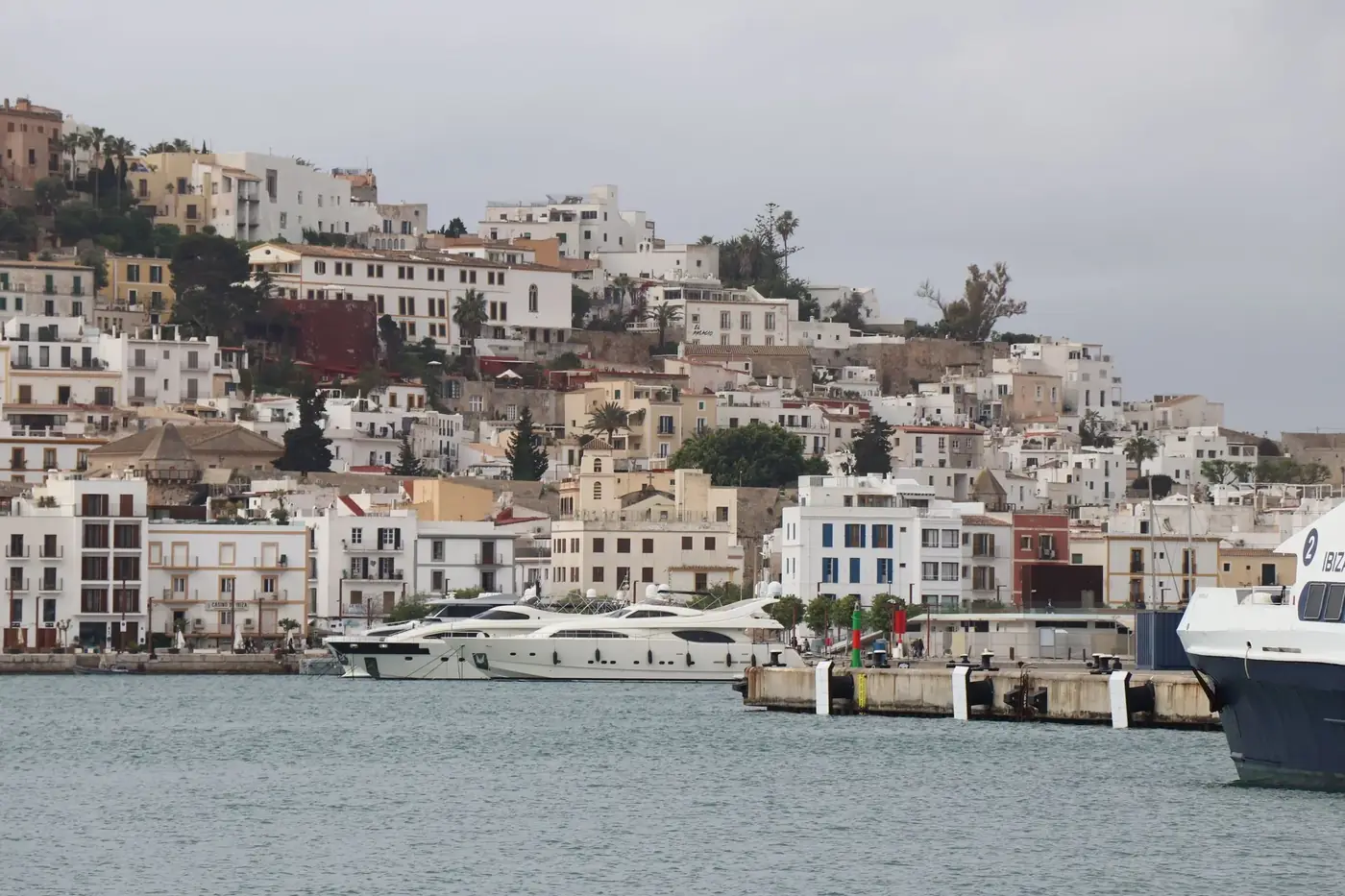 Panoramic view of Ibiza's old town architecture and luxury yachts in the marina, Balearic Islands.