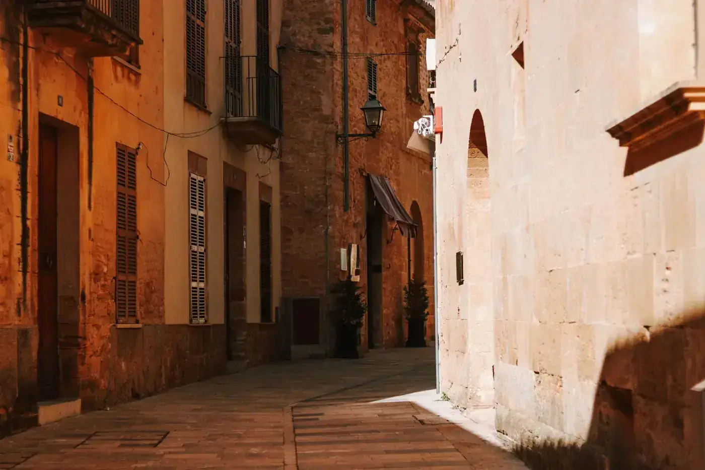 Sunlit narrow alleyway with rustic buildings in Mallorca, Spain, showcasing traditional architecture.