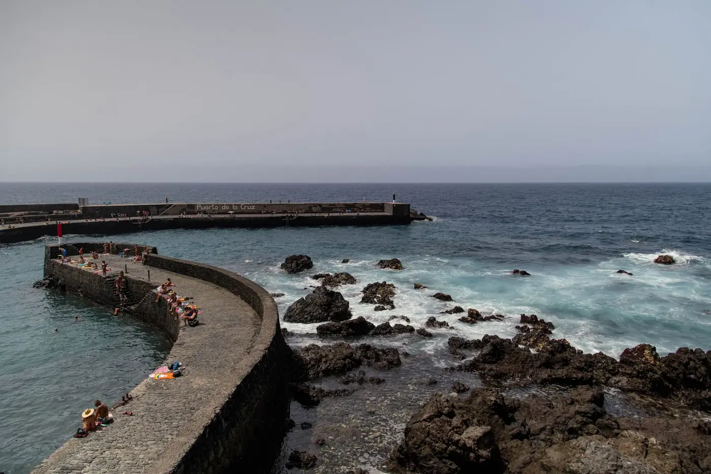 A beautiful summer day at the rocky coastline of Puerto de la Cruz, Tenerife, with people enjoying the ocean view.