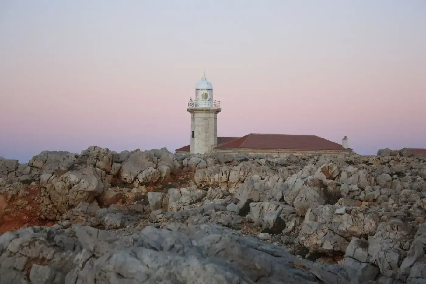 Scenic sunset view of Punta Nati Lighthouse surrounded by rocky terrain in Menorca, Spain.