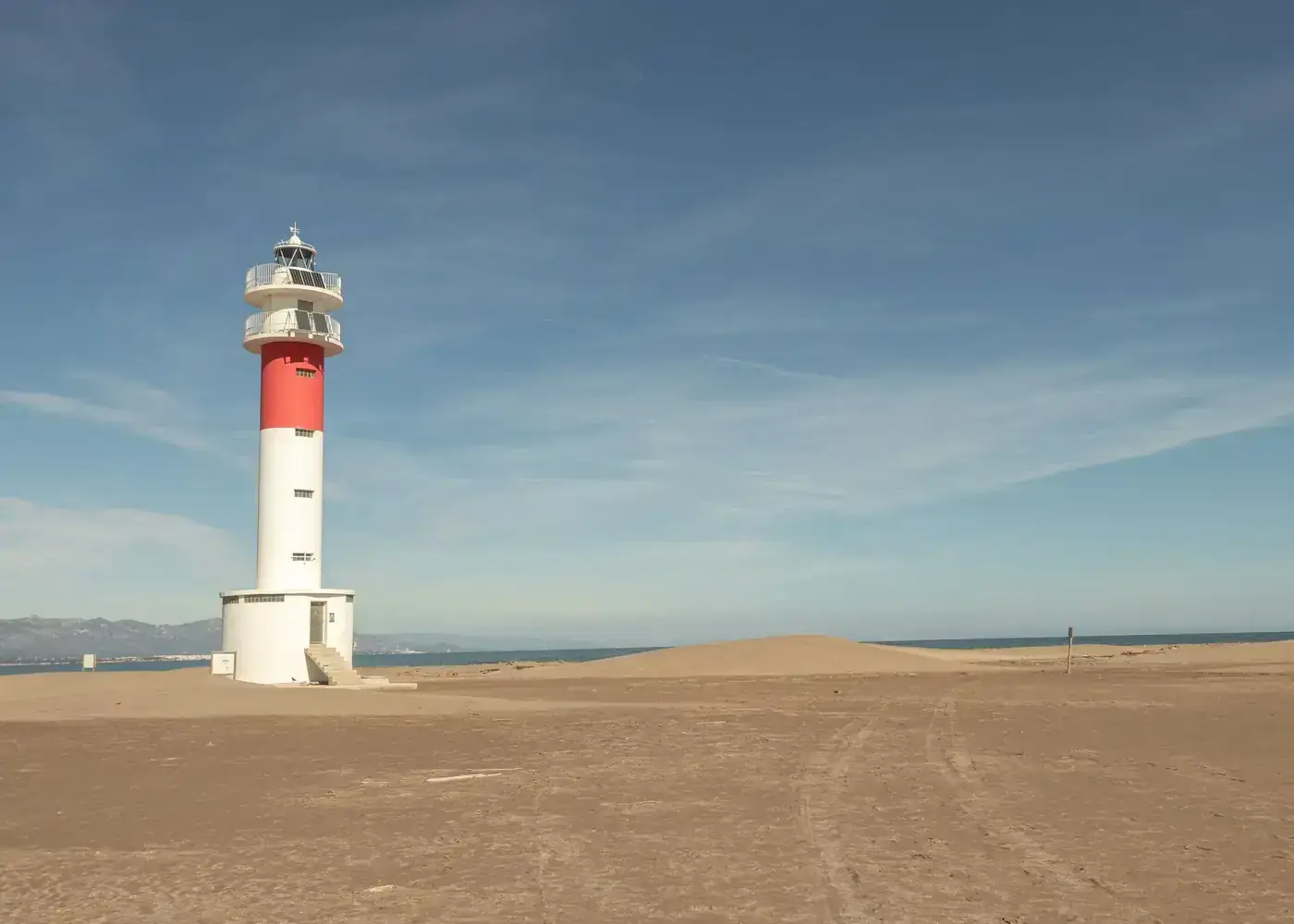 Lighthouse standing tall on a sandy beach under a clear blue sky.
