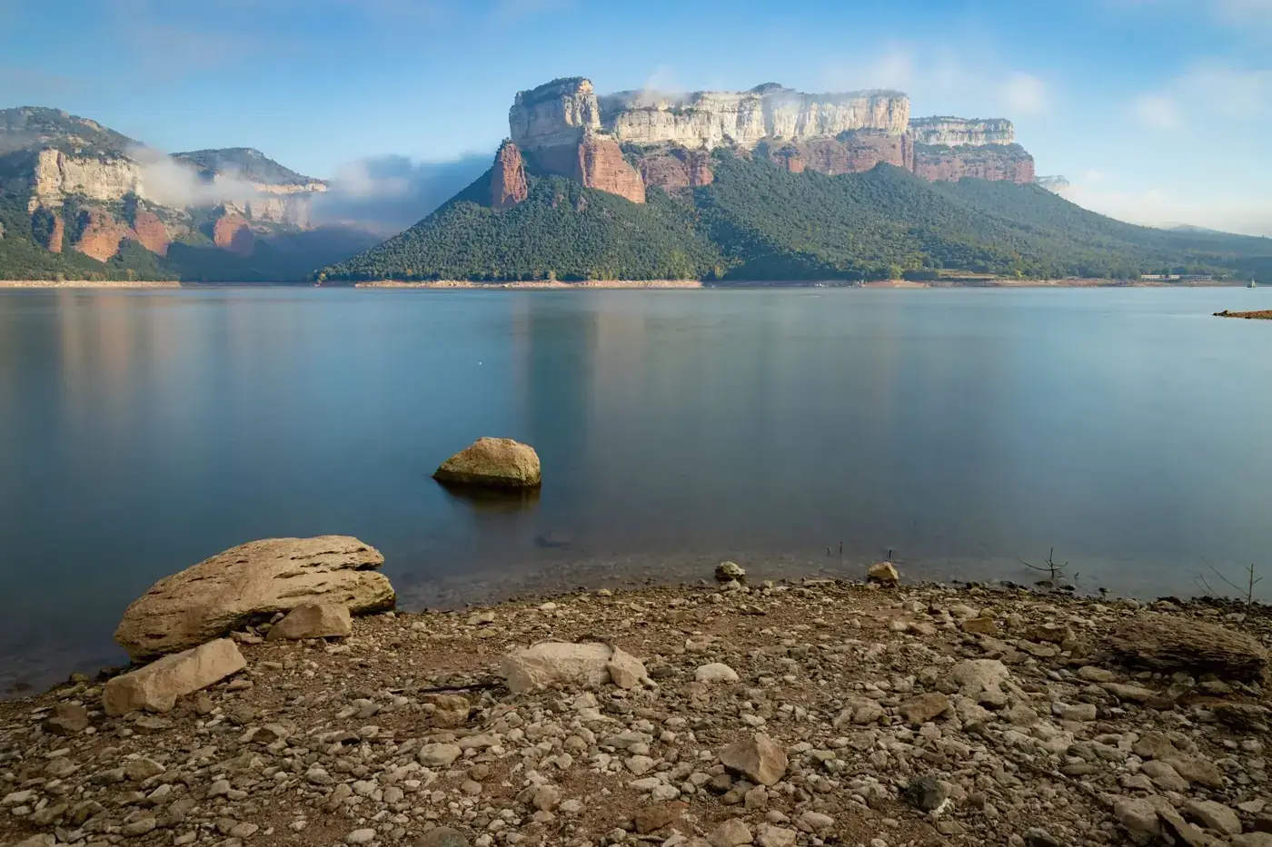 Tranquil scene of Sau Reservoir with majestic mountains under clear skies.
