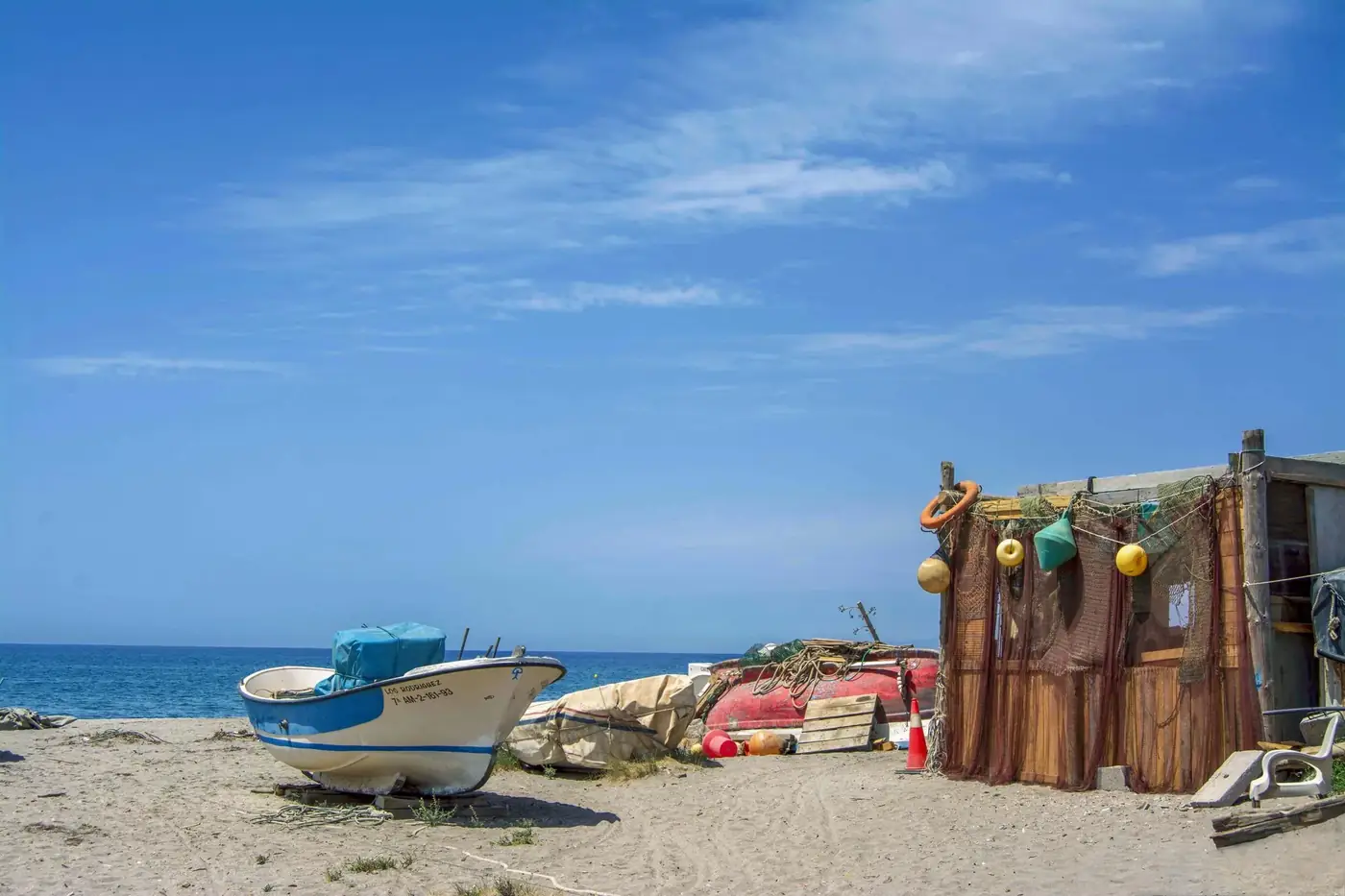 Peaceful beach scene with a fishing boat and rustic cabin in Cabo de Gata, Spain.