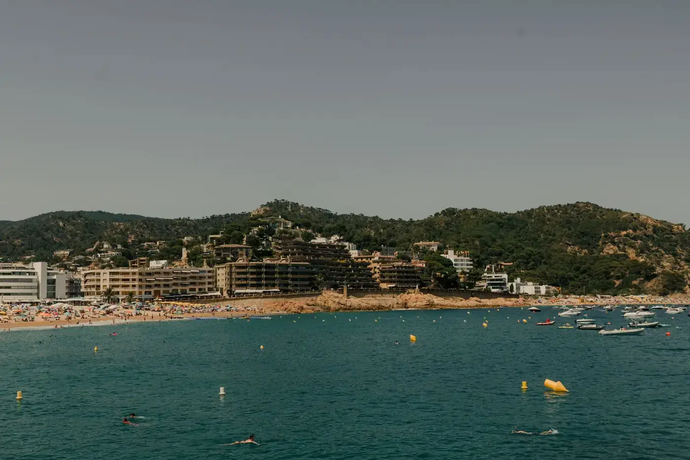 Captivating view of Tossa de Mar's beach with sunbathers and boats on a sunny day.