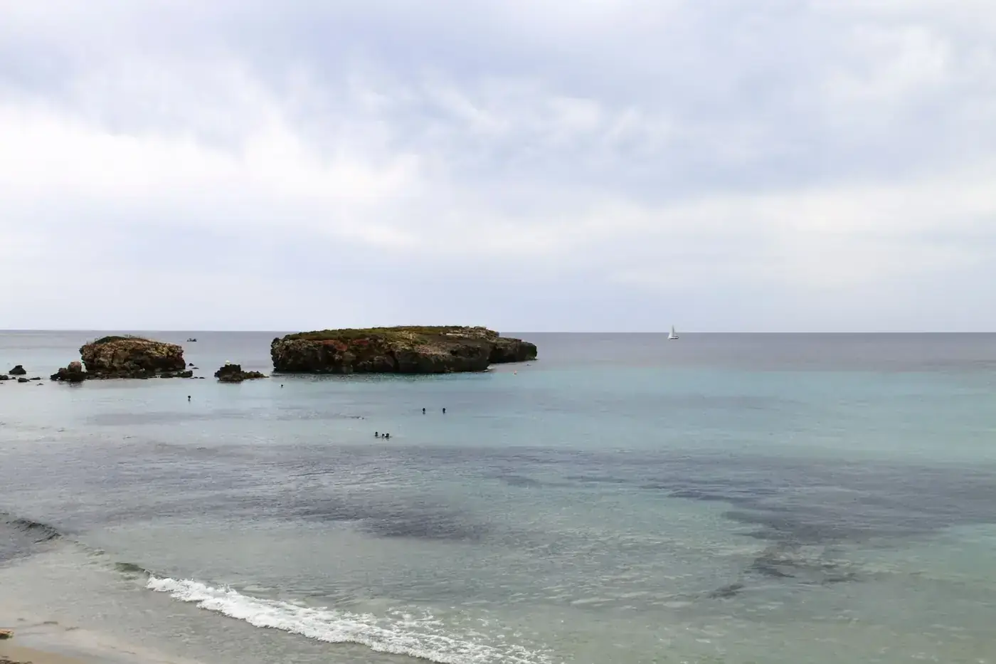 Serene view of the Mediterranean Sea near Ciutadella de Menorca with scattered islets and a distant sailboat.
