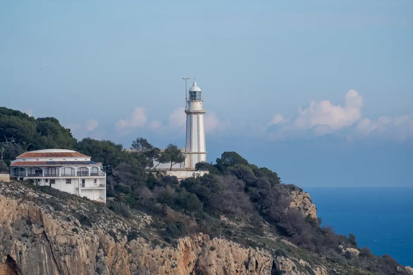 A stunning view of Cap de Sant Antoni Lighthouse perched on rocky cliffs overlooking the Mediterranean Sea in Jávea, Spa