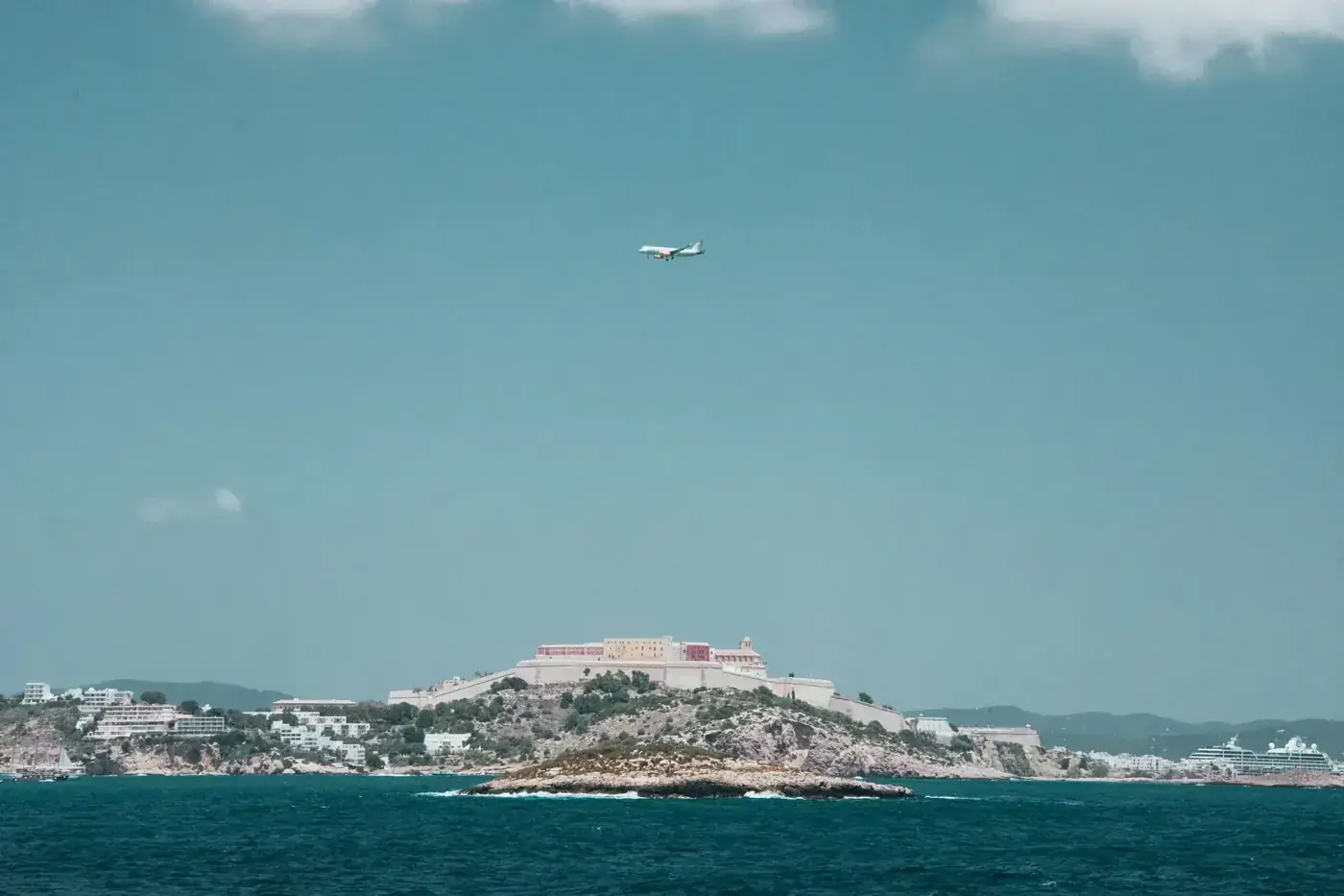 Scenic view of Ibiza's coastline with an airplane flying over the Mediterranean Sea.