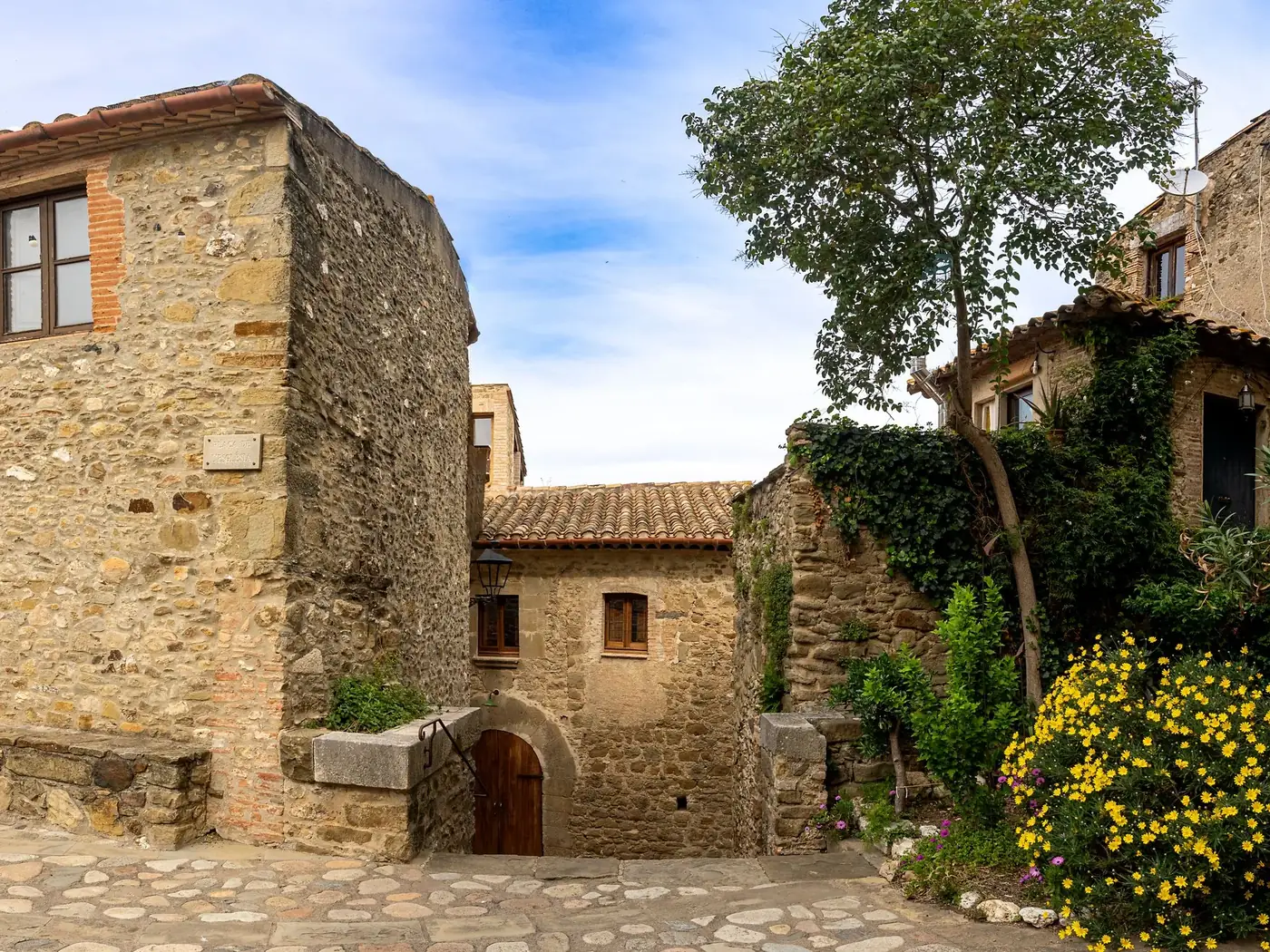 Rustic stone houses and cobblestone streets in Sant Martí Vell, Spain surrounded by lush flora.