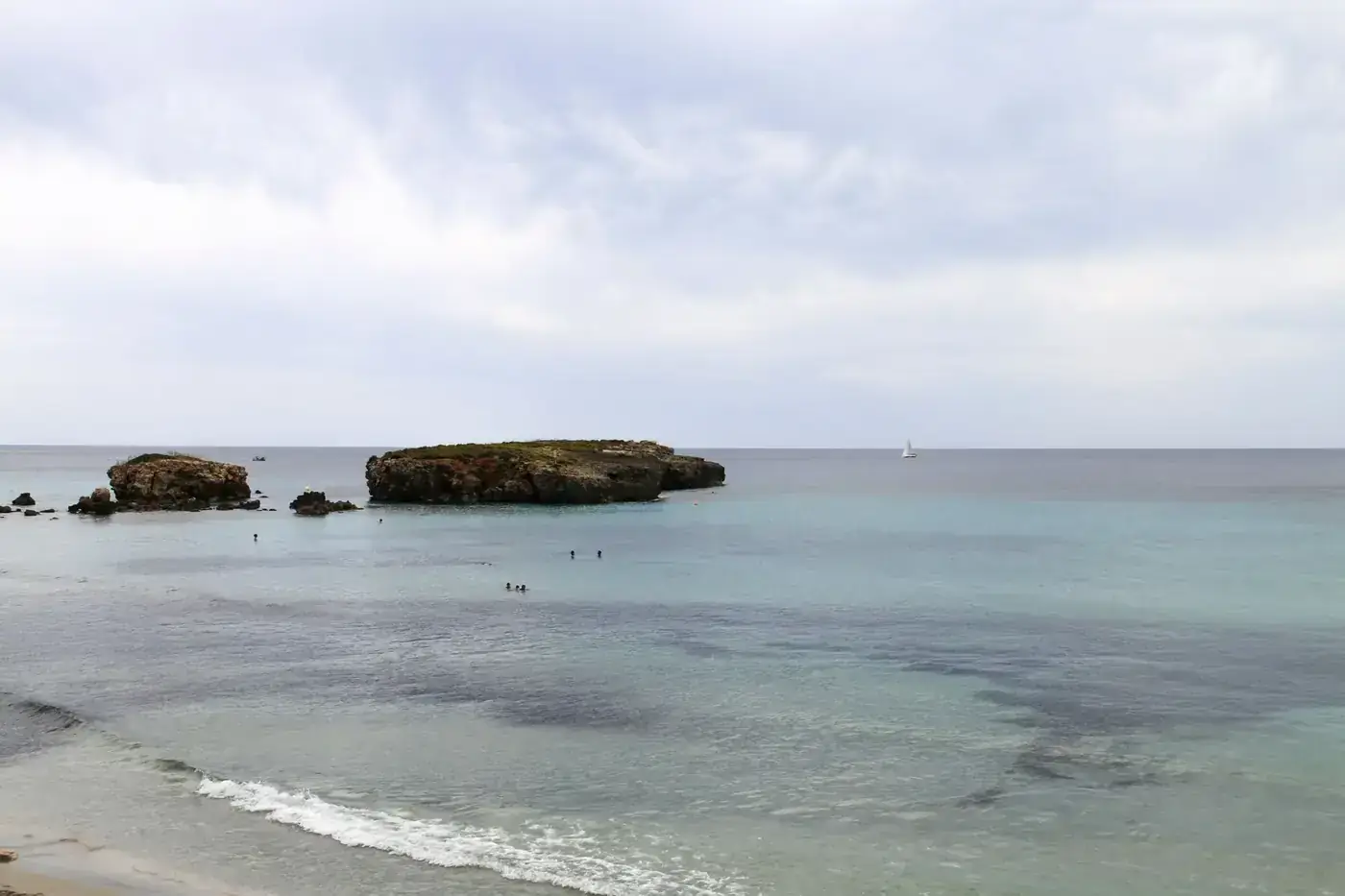 Serene view of the Mediterranean Sea near Ciutadella de Menorca with scattered islets and a distant sailboat.