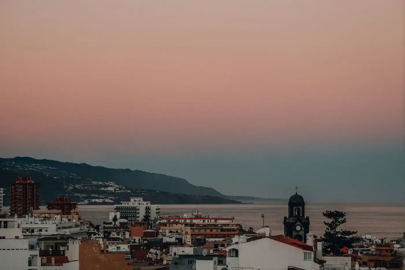 A serene twilight view of a coastal city with an ocean backdrop and pastel skies.