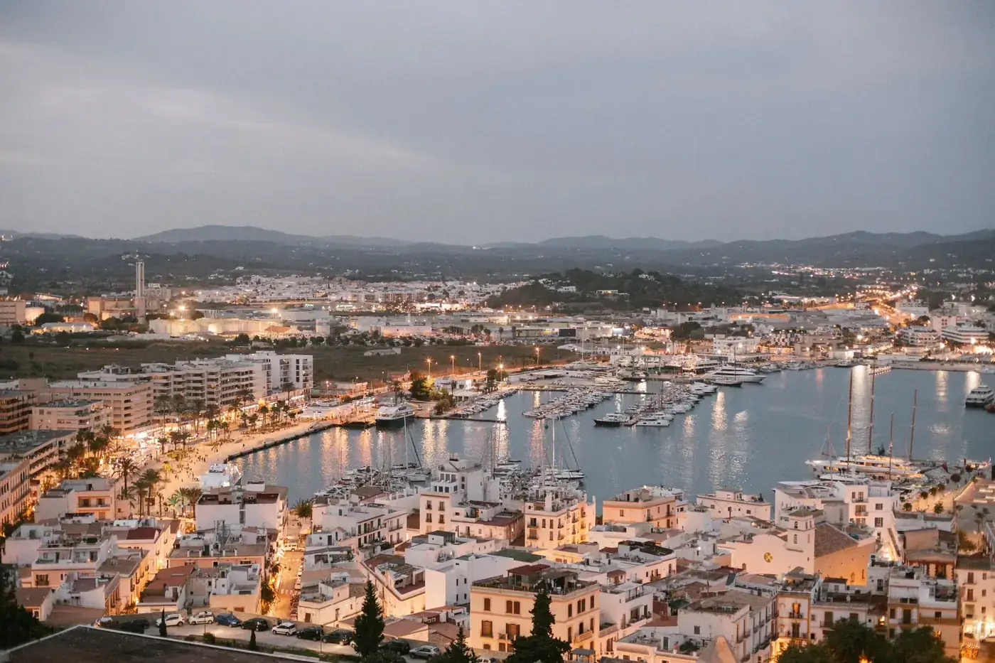 A scenic aerial view of Ibiza's marina at dusk, showcasing vibrant city lights and bustling harbor in Spain.
