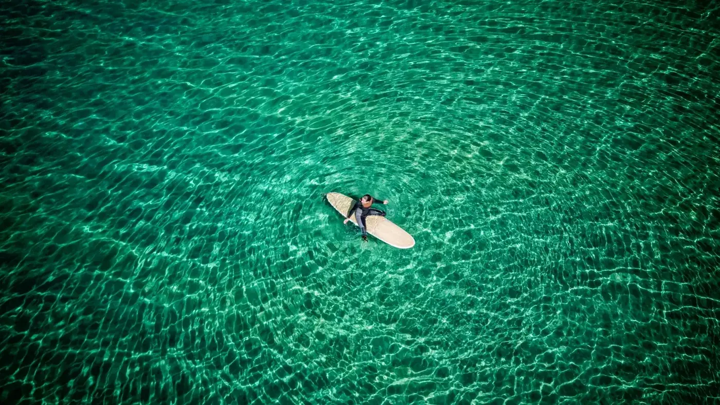 Aerial view of a surfer girl waiting for a wave at a paradise beach in Galicia, Spain.