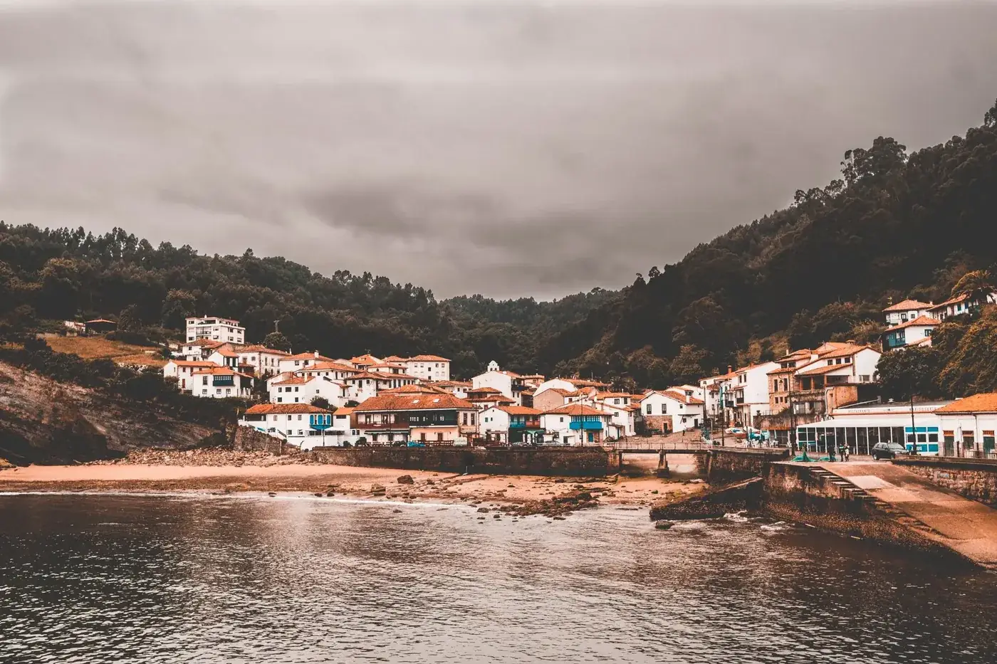 Charming coastal town of Candás, Spain under overcast skies with traditional houses along the waterfront.