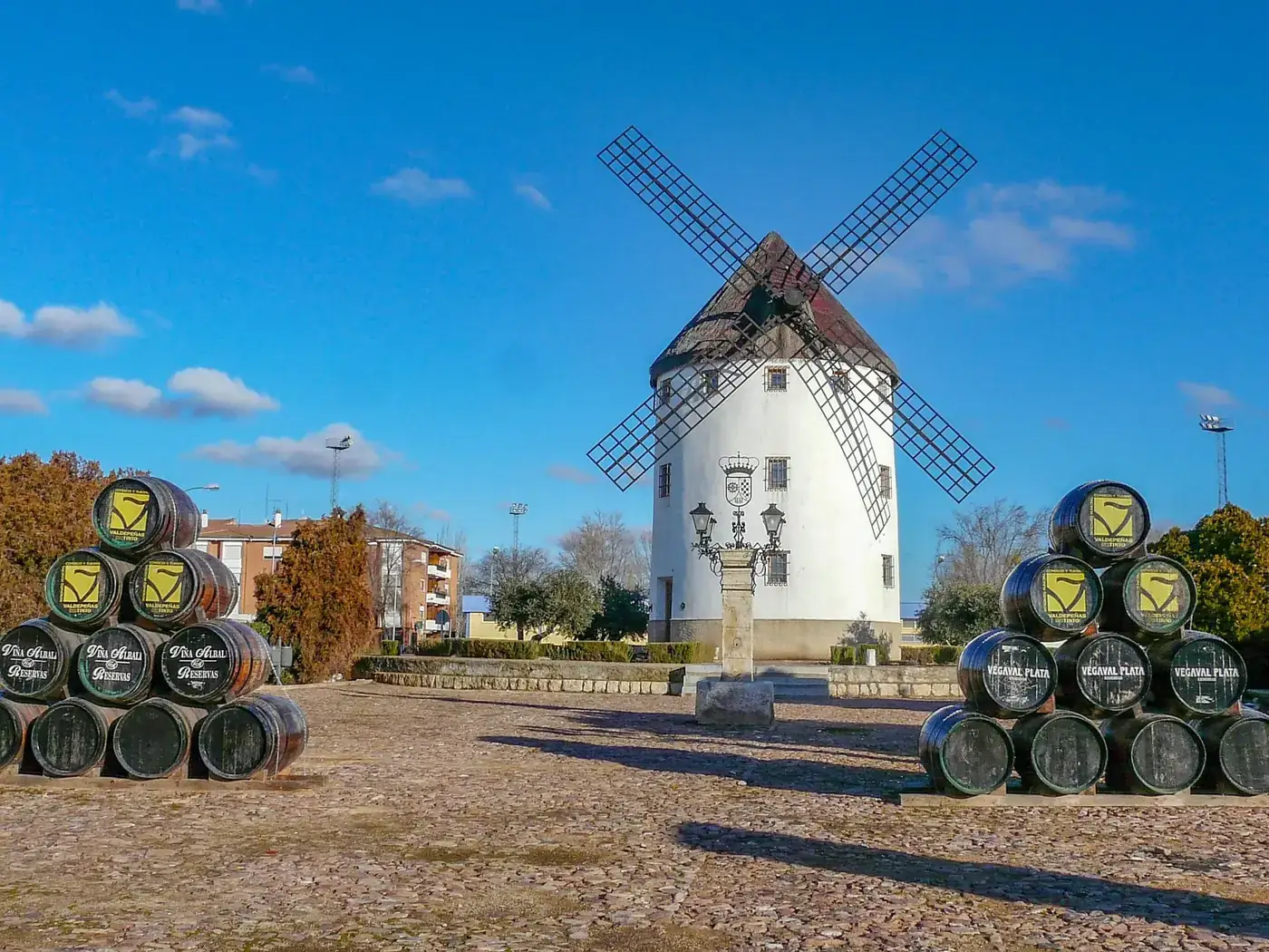 Charming windmill with stacked wine barrels in Campo de Criptana, Spain under a clear blue sky.