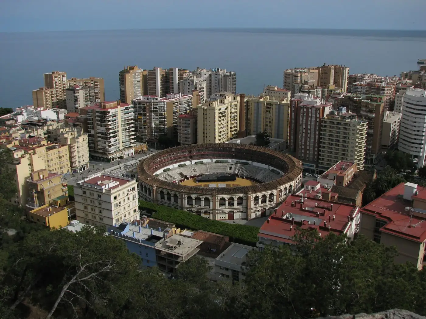 Aerial capture of Malaga's bullring surrounded by modern buildings and Mediterranean Sea.