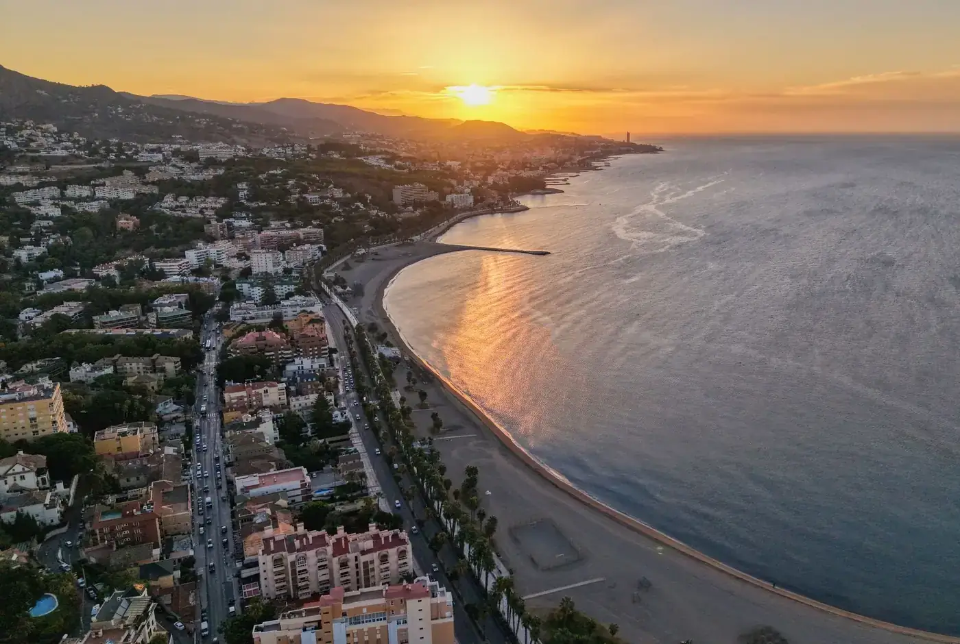 A breathtaking aerial view of Málaga's coastline at sunset, showcasing vibrant city life and serene beach views.