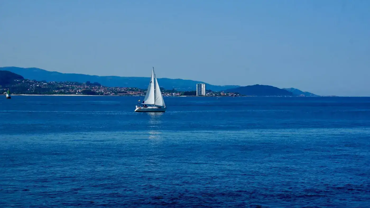 A tranquil scene of a sailboat gliding across the blue waters of Vigo Bay, Spain.