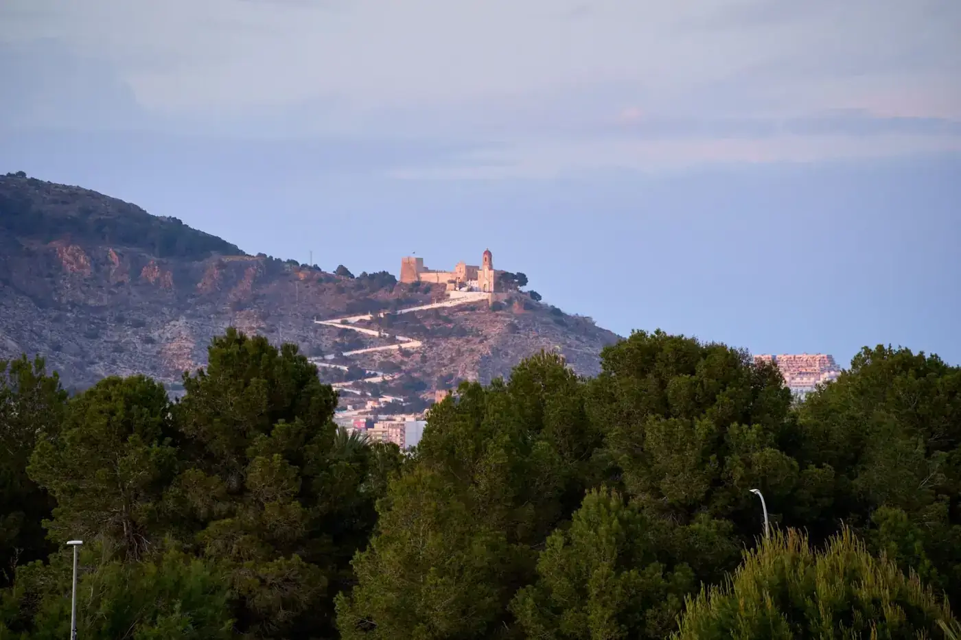 Picturesque view of Cullera Castle on a hillside at sunset, surrounded by lush greenery.