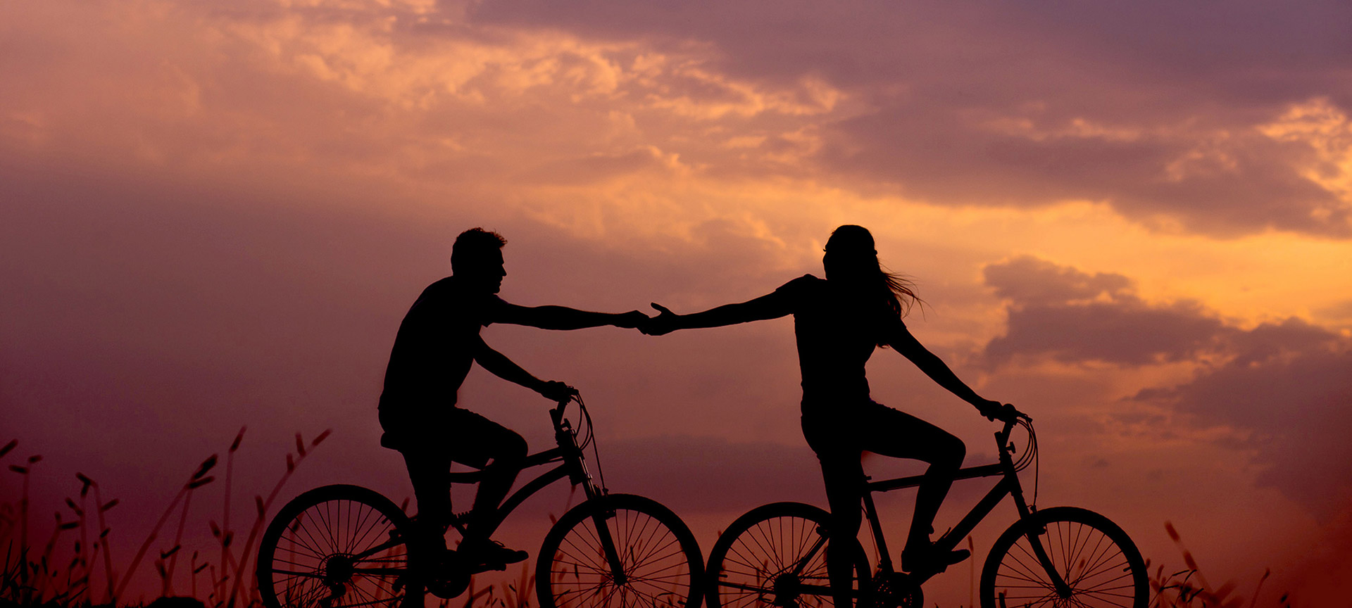 Twee fietsers hand in hand bij zonsondergang.