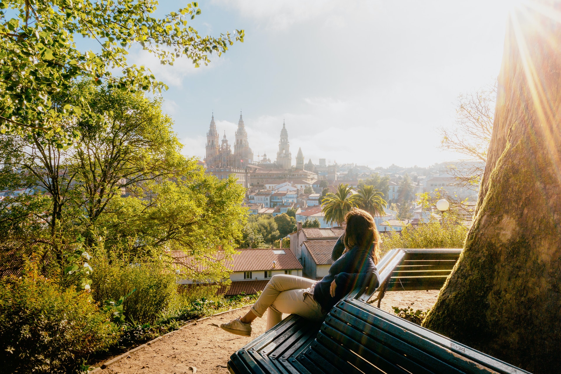 Vrouw op een bankje in het park kijken naar de kathedraal van Santiago de Compostela bij zonsopgang, park en zonnige hemel