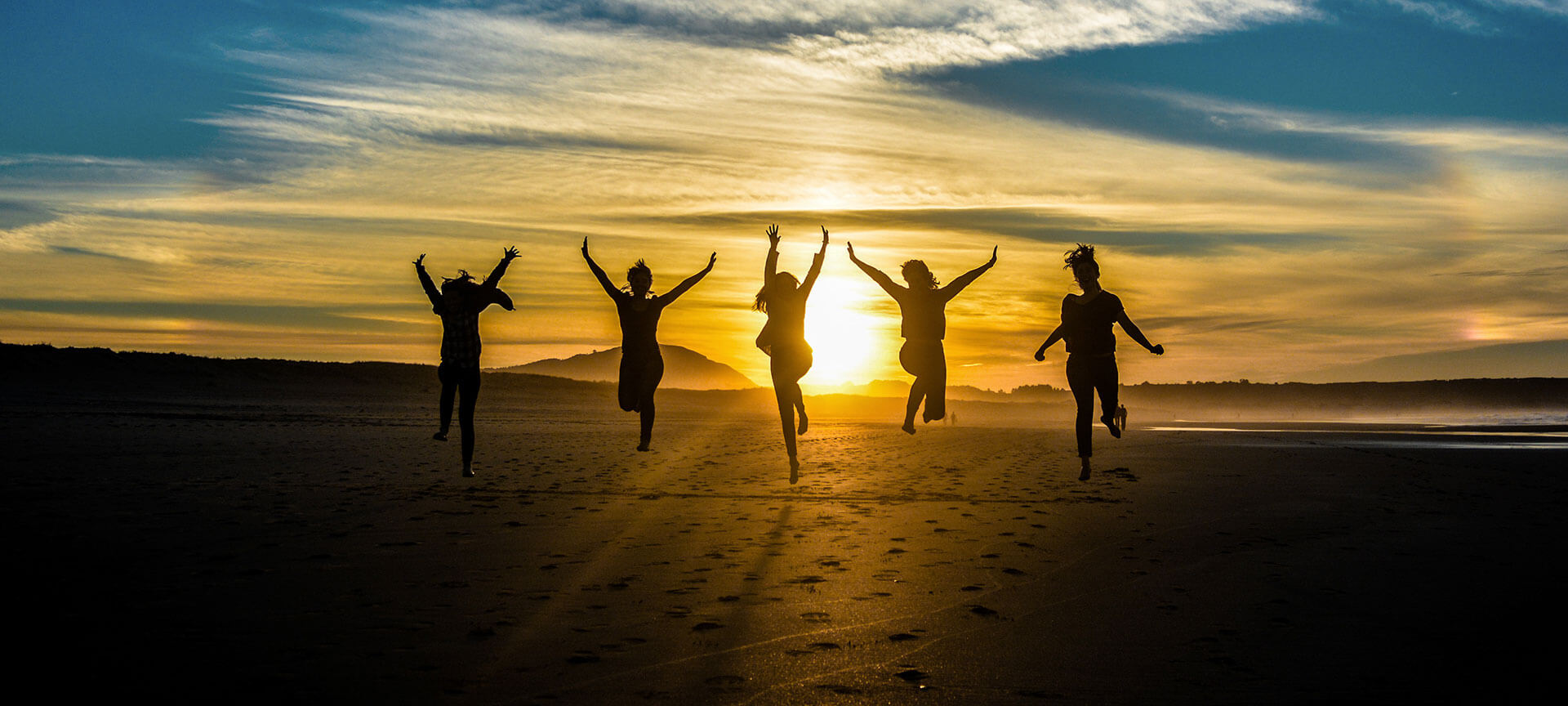 Springende mensen tijdens zonsondergang op strand.