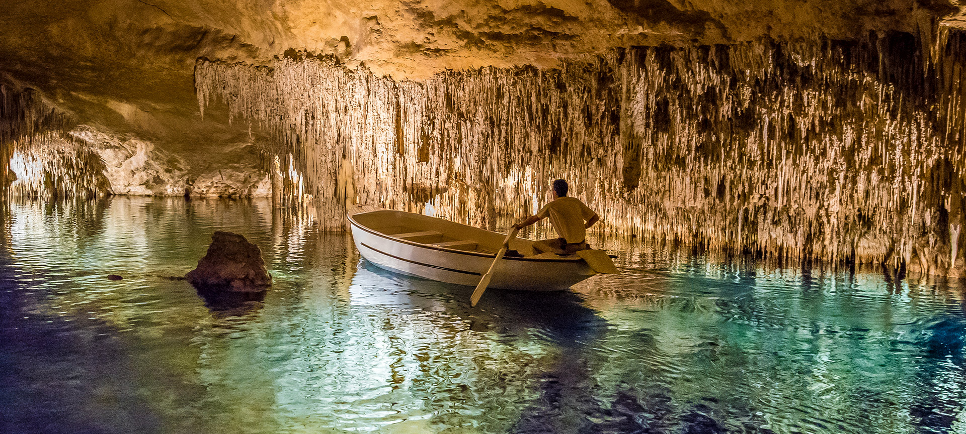 Persoon roeit in ondergrondse grot met stalactieten.