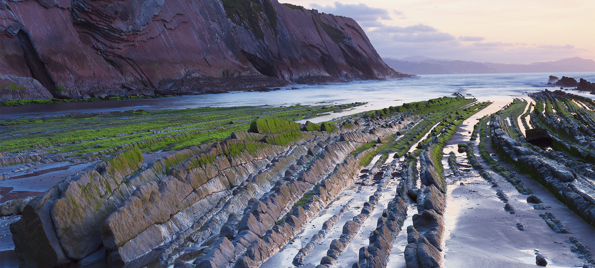 Geërodeerde rotsformaties aan kustlijn bij zonsondergang.